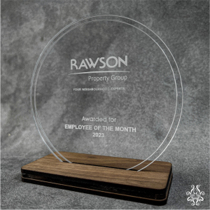 Acrylic employee of the month award with a wooden base, engraved for Rawson Property Group, showcasing a circular design and sleek, modern aesthetic against a grey background.