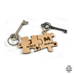 Laser-cut puzzle piece keychains with personalized initials 'J' and 'M,' engraved alongside the date '01.09.21,' interlocked together, attached to vintage keys.