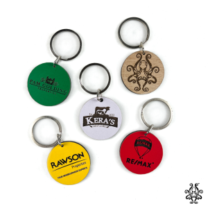 Set of five customizable corporate keychains in green, white, natural wood, yellow, and red, each engraved with a company logo.